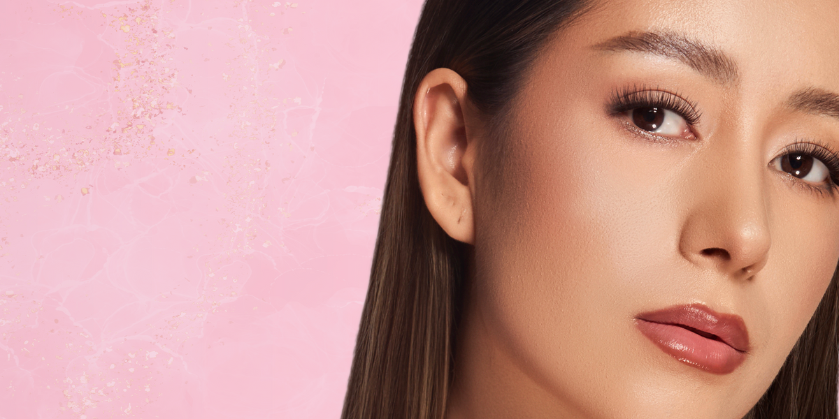 Beauty portrait of a woman with styled upper lashes against a pink textured background.